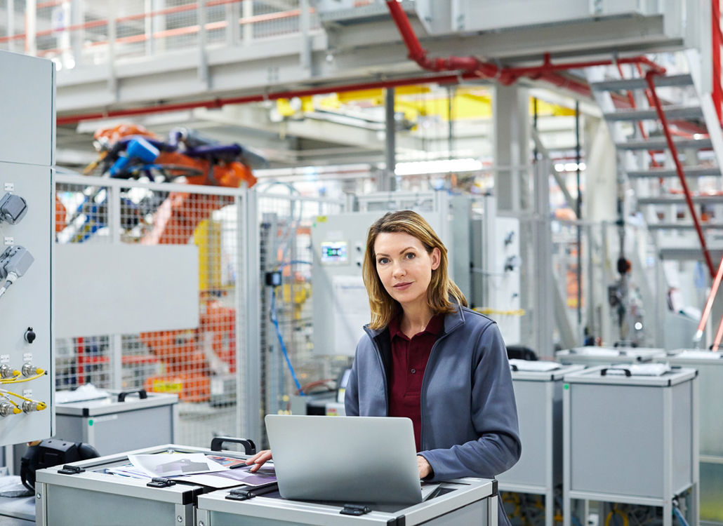 En självsäker kvinnlig ingenjör arbetar på en bärbar dator i en modern industrifabrik och övervakar automatiserade produktionssystem.